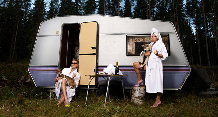 En man sitter framför en husvagn i en vit morgonrock. Bredvid står en kvinna i en vit morgonrock.