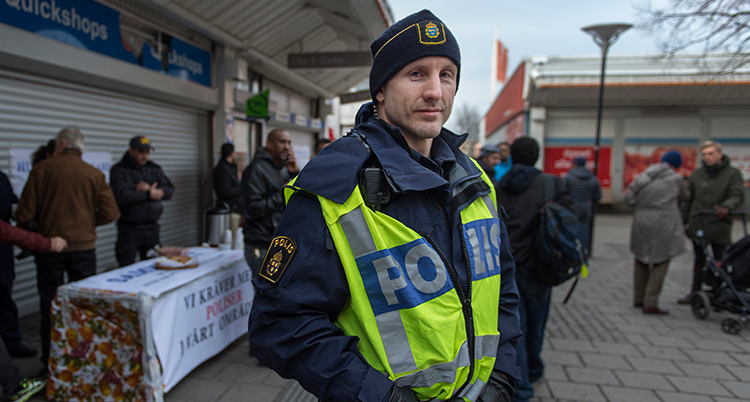 En man i gul polisväst står på ett torg.