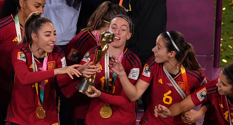 De har röda fotbollströjor och är glada. De står nära varandra och håller i en pokal.