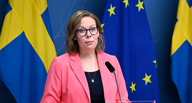 Hon har rosa kavaj. Hon står framför en mikrofon.