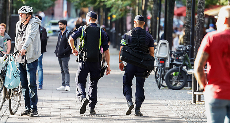 Två poliser bakifrån. De går på en trottoar i Stockholm.