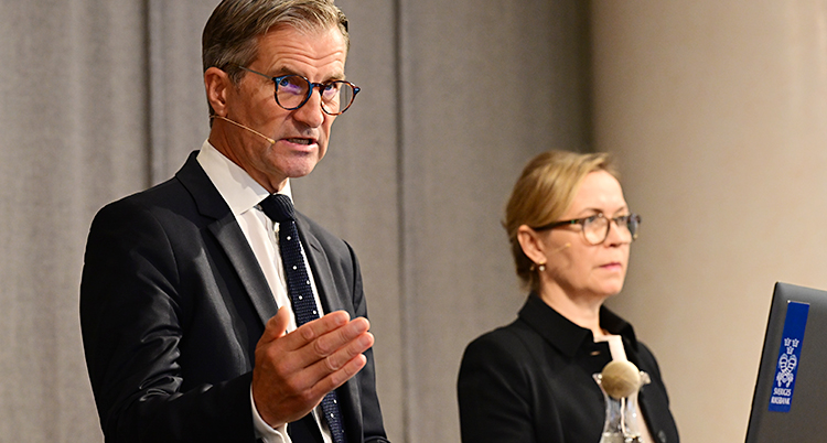 Erik och Åsa står vid ett bord och pratar till journalister.