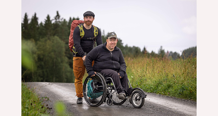 Linuas står bakom rullstolen som Anders sitter i. De står på en grusväg.