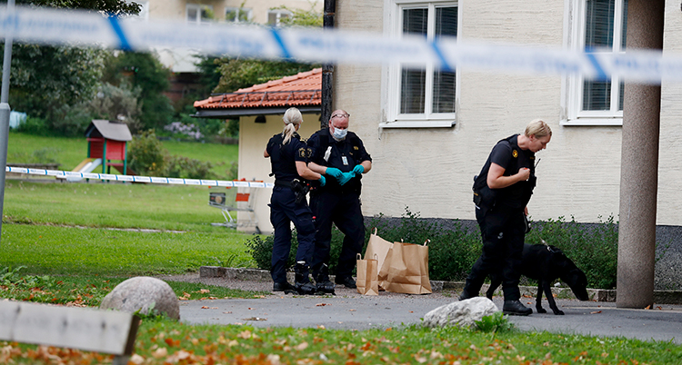 Poliser undersöker platsen utanför ett hus med lägenheter.