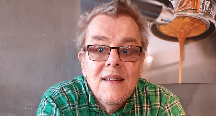 Ett nära porträtt. Han tittar in i kameran. Han har glasögon.