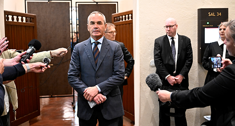 En man i kostym omgiven av journalister.