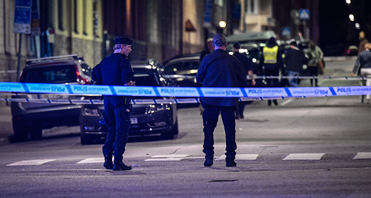 Två poliser står på gatan. De har spärrat av platsen med tejp.