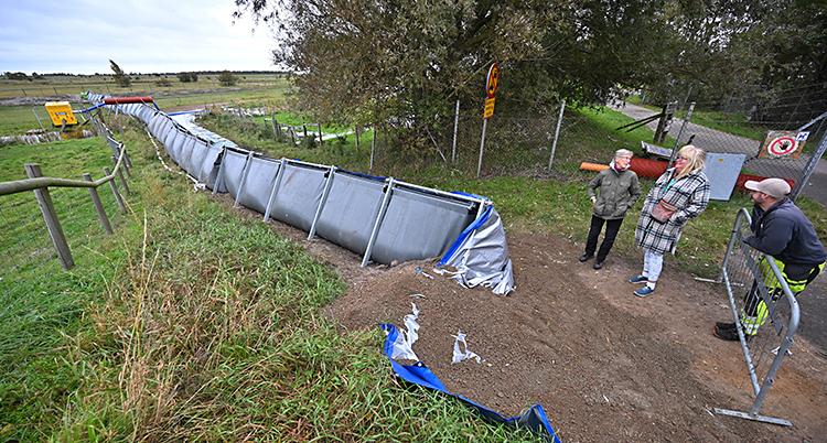 En bild från Skanör. Tre personer står vid en lång vall som har byggts på en åker.