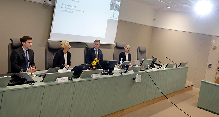 Fyra personer sitter bakom ett långt bord. De har mikrofoner.