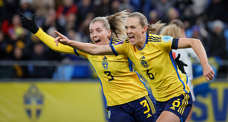 De har gula fotbollströjor. De springer intill varandra och sträcker upp varsin arm mot luften. De är glada.