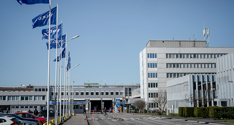 Fabriken i Göteborg. Flaggor och en bilparkering syns.