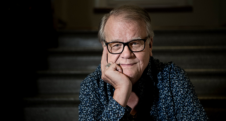 Han har glasögon och tittar in i kameran.