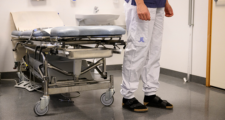 Två ben på personal i vården bredvid en sjukhussäng.