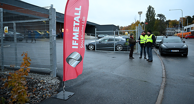 Några personer i varselväst står vid grindarna in till ett verkstadsområde.