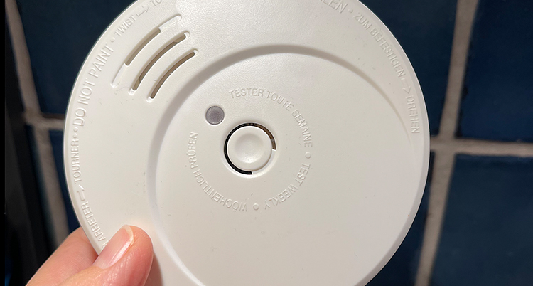 En hand håller på en brandvarnare som sitter i taket.