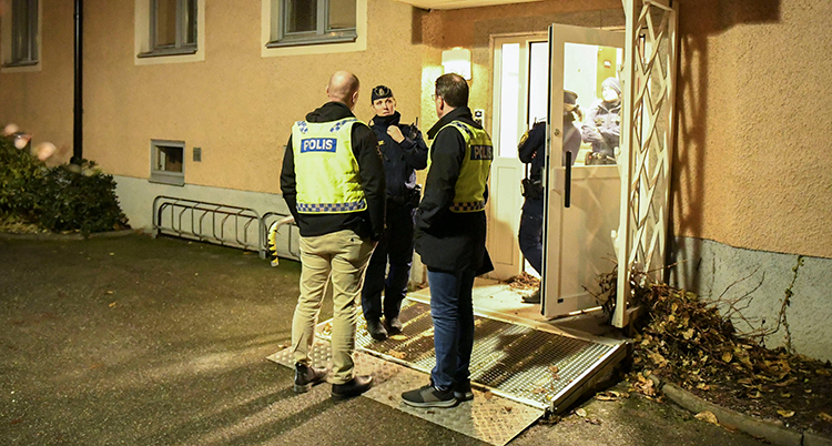 Tre poliser pratar utanför en entré till ett flerbostadshus.