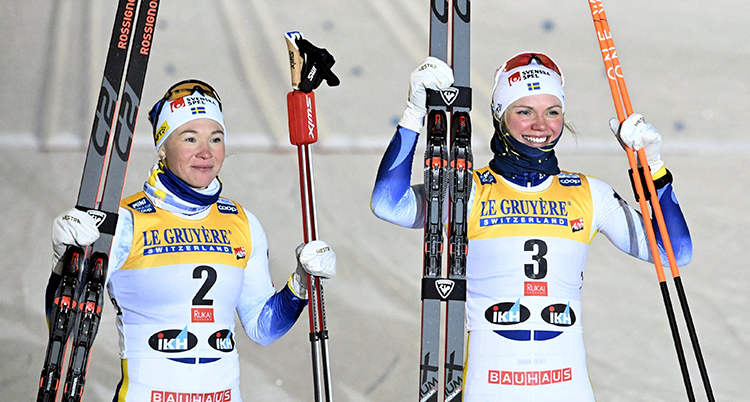 De håller upp sina skidor och stavar och är glada.