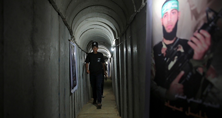 Han går i en smal tunnel. På väggen finns en målning med en palestinsk soldat.