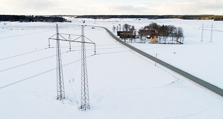 Stora ledningar med el som går över ett fält. Där syns ett hus i bakgrunden.