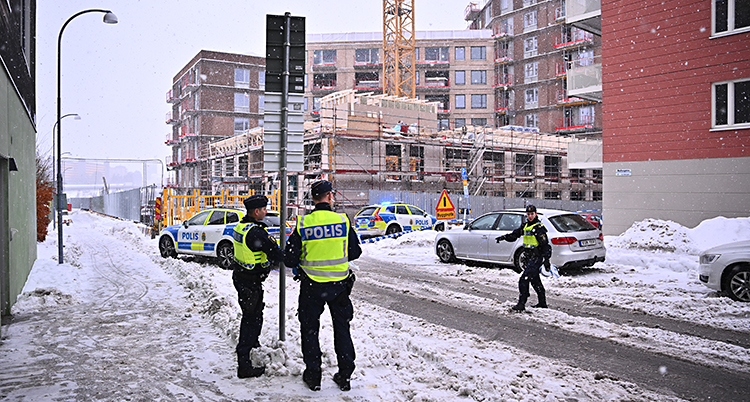 Flera poliser och flera polisbilar står utanför ett bygge.