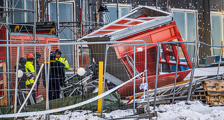 En kraschad bygghiss ligger på marken. Några personer står vid sidan om.