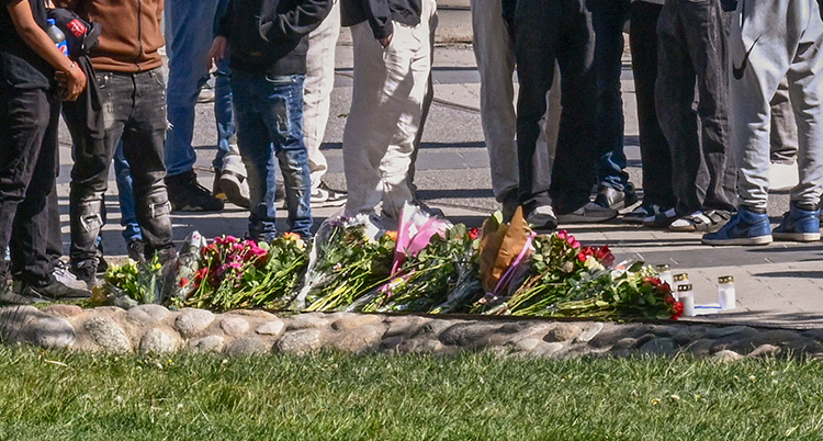 Flera personer står vid en hög med blommor. Man ser bara deras ben.