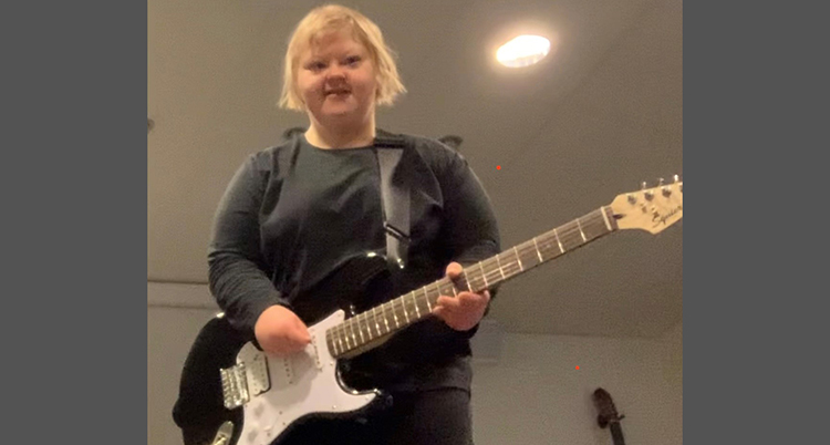 Hon står upp och spelar på en svart elgitarr.