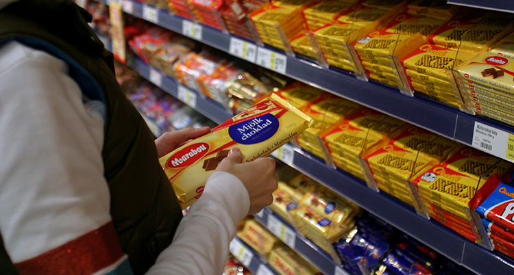 En person står vid en hylla med choklad. Hen håller i en chokladkaka från Marabou.