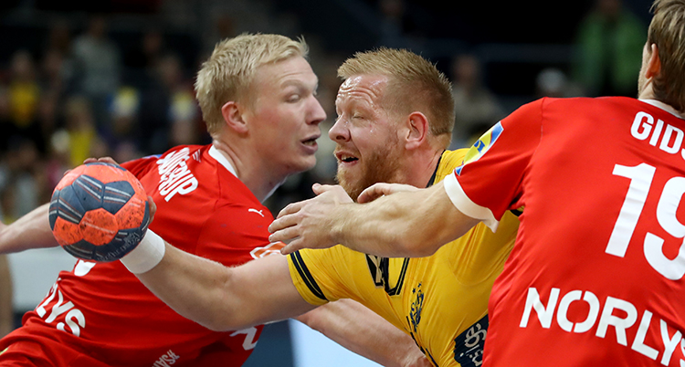 Han kämpar för att komma förbi två spelare med röda tröjor.
