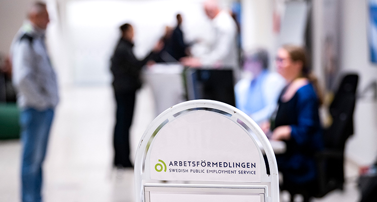 Suddiga människor bakom en skylt med Arbetsförmedlingen.
