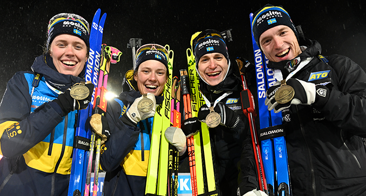 Fyra personer i skidkläder är glada och visar sina medaljer.