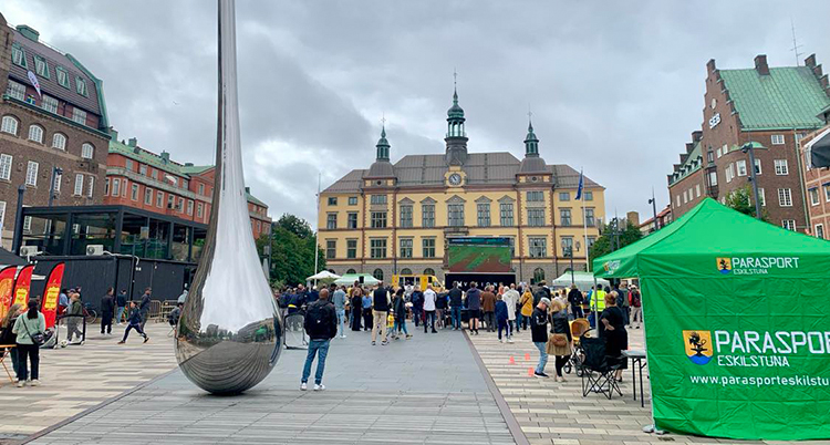 Ett torg med många människor. Längst bort syns ett stort gult hus.