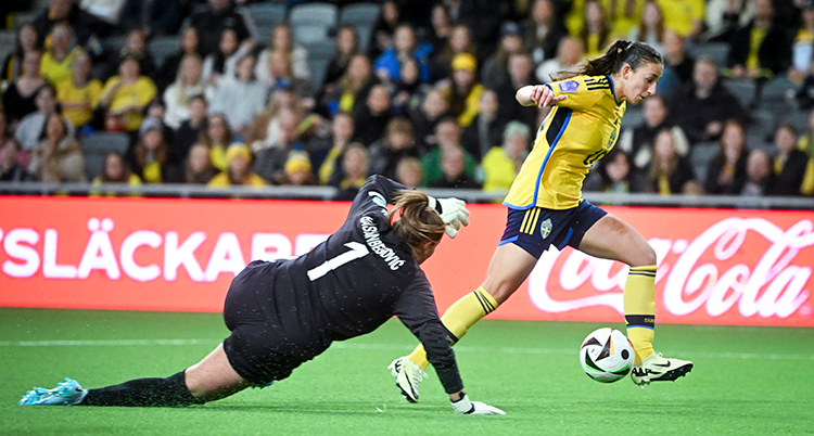 Målvakten har kastat sig och en spelare med bollen är på väg förbi.