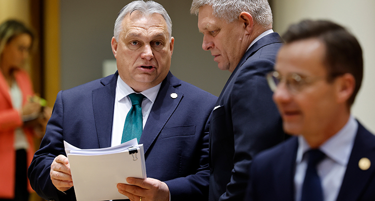 Han håller ri papper och pratar med en annan man. Längst fram syns Sveriges statsminister lite suddigt.