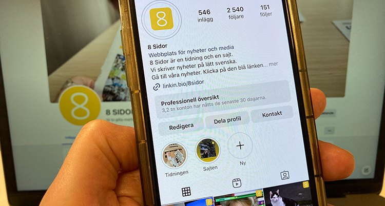 En hand håller i en mobiltelefon framför en dator.