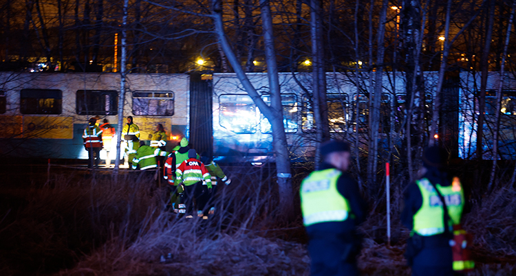 Det är mörkt ute. En spårvagn syns i fonden. Framför jobbar poliser i gula västar.