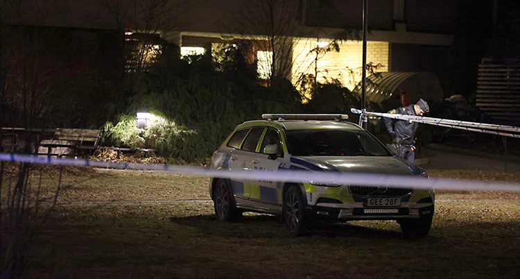 Det är mörkt. En polis går runt på en gräsmatta. En polisbil står bredvid.