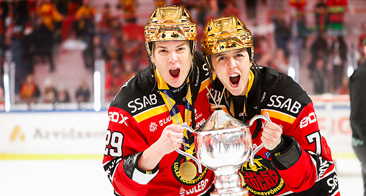 Två spelare står på isen och jublar. De håller i en pokal och har guldhjälmar på huvudet.