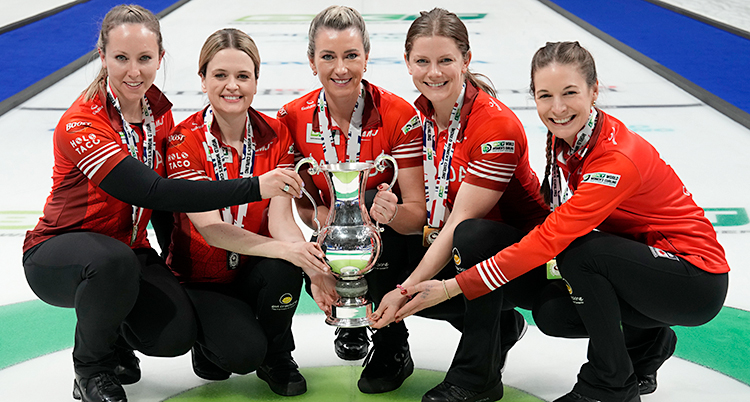 Fem kvinnor sitter på huk och håller i en pokal. De är glada.