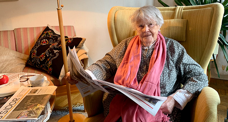 Hon sitter i en fåtölj. Hon bläddrar i tidningen 8 Sidor.