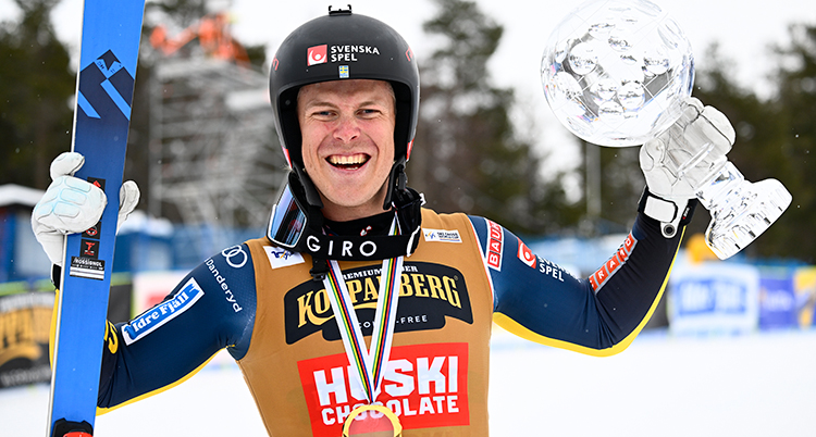 Han är glad. Han har en medalj om halsen och håller skidor och en glasvas i händerna.