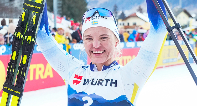 Hon är glad och sträcker upp armarna med skidor och stavar.