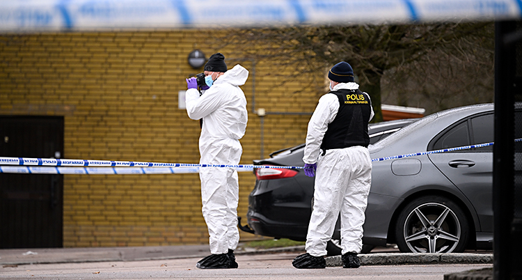 Två poliser står på en parkering. En av dem fotograferar.