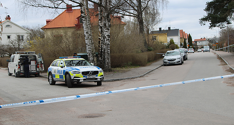 Ett bostadsområde med villor. Poliserna har spärrat av med band. Innanför banden är flera polisbilar.
