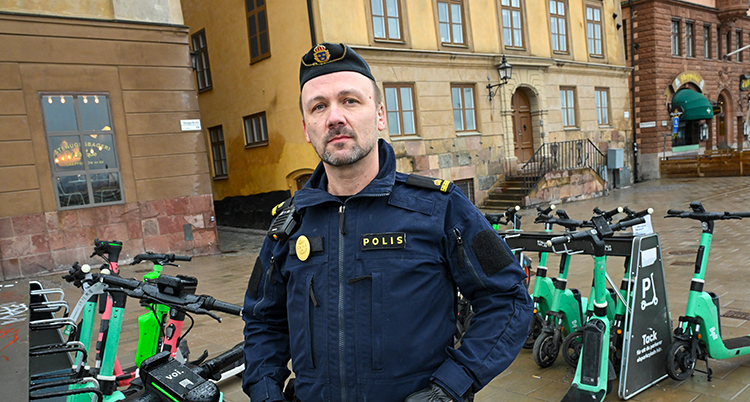 Han har poliskläder. Han står framför elsparkcyklar.