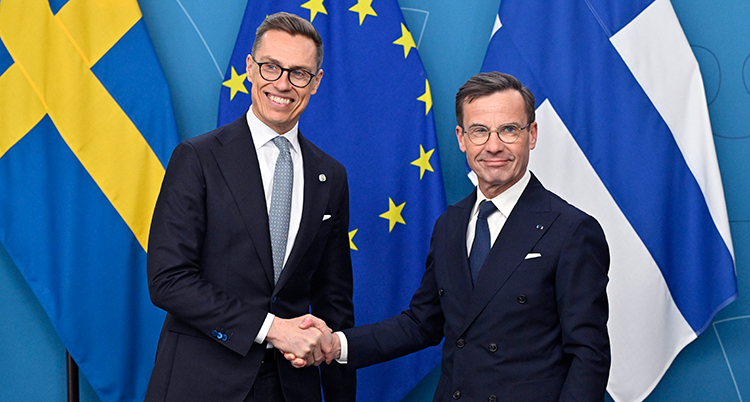 De är glada och skakar hand framför Sverige, Finlands och EUs flaggor.
