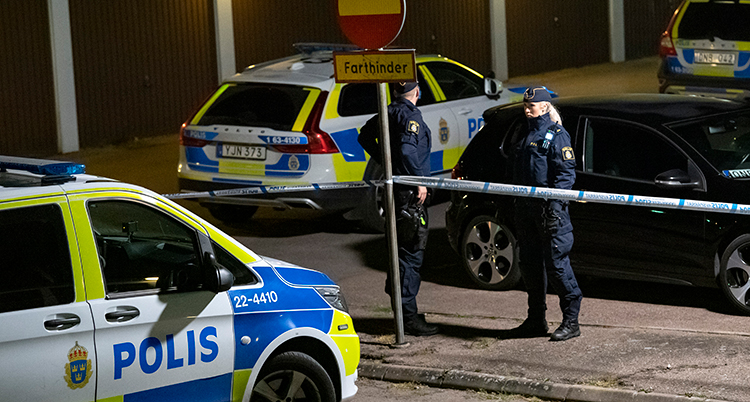 Två poliser står vid polisbilar och blå band.