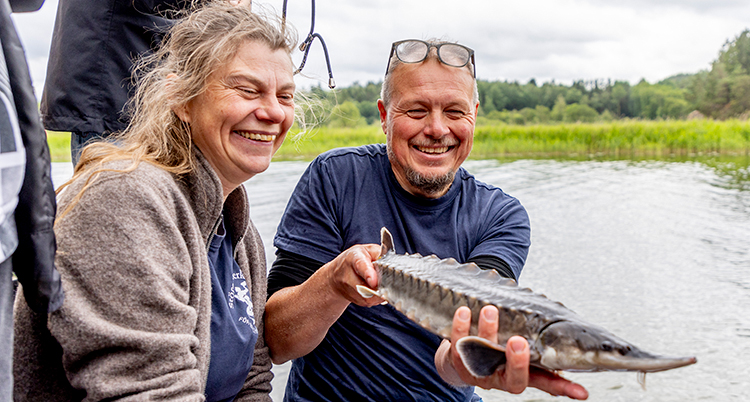 De är intill varandra vid en flod. Han håller i fisken.