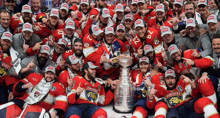 Många glada spelare sitter på isen med en stor pokal i mitten.