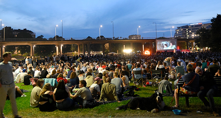 Massor av människor har samlats i en park. De tittar på film på en stor skärm.
